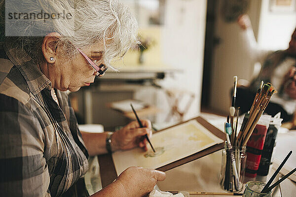 Ältere Frau malt zu Hause mit Pinsel