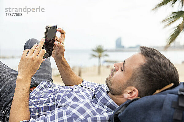 Reifer Mann mit Handy entspannt am Strand