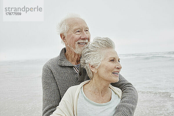Glückliches älteres Paar  das lächelnd am windigen Strand steht