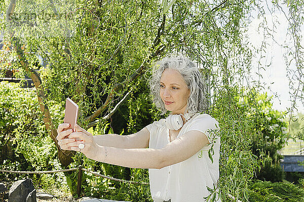 Lächelnde Frau macht Selfie mit Smartphone im Park
