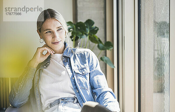 Junge Geschäftsfrau in Jeansjacke sitzt an einem sonnigen Tag im Büro