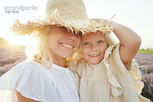 Smiling cute girl with mother wearing hat in field