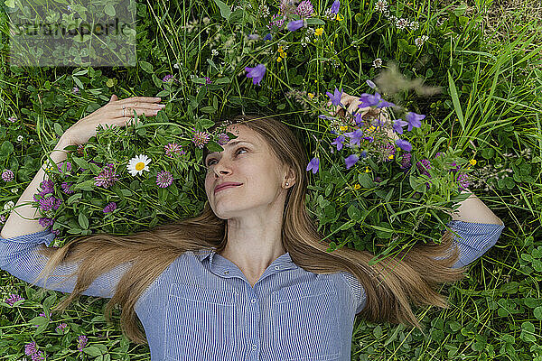 Lächelnde Frau liegt inmitten von Blumen auf dem Feld