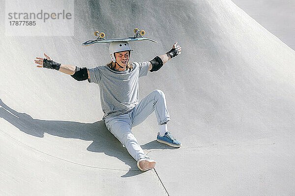 Glücklicher Mann balanciert Skateboard auf dem Kopf im Skatepark