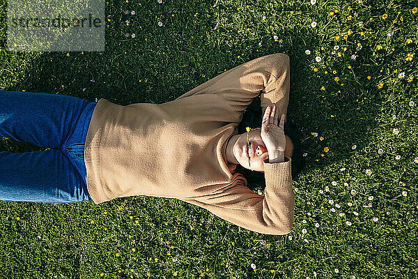 Young woman lying with hand covering eyes on grass at park