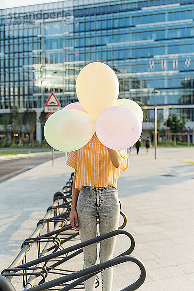 Frau bedeckt Gesicht mit Luftballons und steht am Fahrradparkplatz