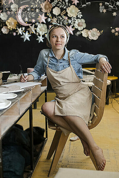 Lächelnder Handwerker mit Schürze sitzt auf einem Stuhl im Kunstatelier