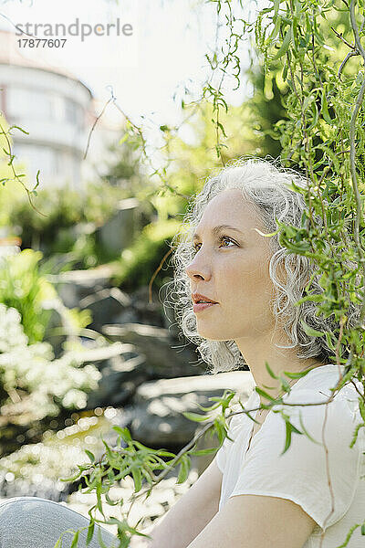 Nachdenkliche Frau sitzt neben Pflanzen im Park