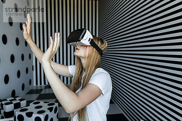 Mädchen mit langen blonden Haaren  das ein Virtual-Reality-Headset trägt und an einer gestreiften Wand gestikuliert
