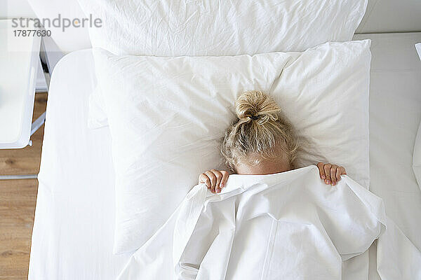 Girl hiding face with blanket in bed