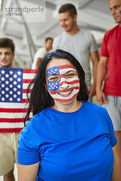 Lächelnde Frau mit amerikanischer Flagge im Gesicht bei Sportveranstaltung im Stadion