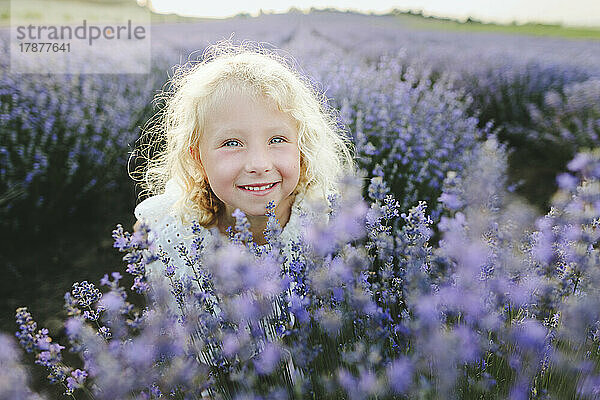 Lächelndes Mädchen mit blonden Haaren inmitten von Lavendelpflanzen