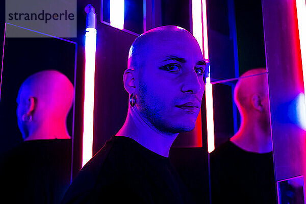 Ernsthaft rasierter Mann in der Nähe beleuchteter Neonlichter