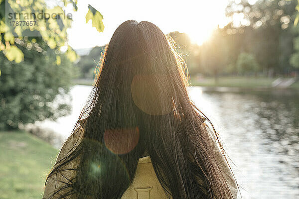 Frau mit langen Haaren blickt auf den See im Park