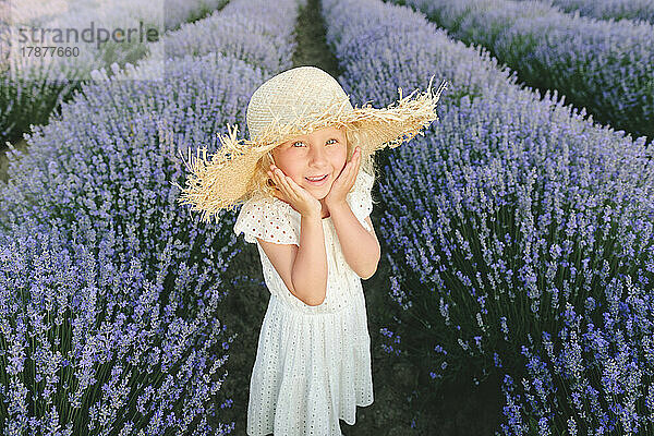 Glückliches süßes Mädchen  das inmitten von Lavendelpflanzen steht