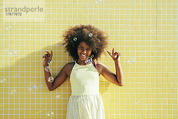 Fröhliches Mädchen mit Afro-Frisur  das ein Friedenszeichen zeigt