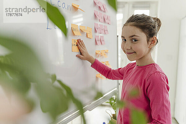 Smiling girl sticking adhesive note on whiteboard at home