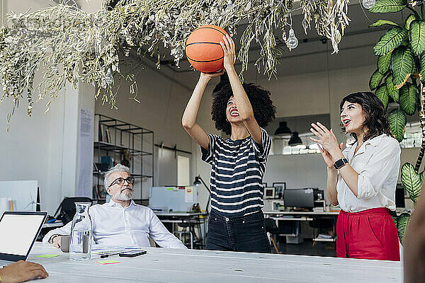Geschäftsfrau spielt Basketball  während Kollege im Büro jubelt