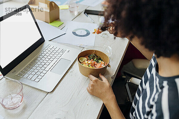 Geschäftsfrau trinkt in der Mittagspause im Büro eine Poke Bowl am Laptop