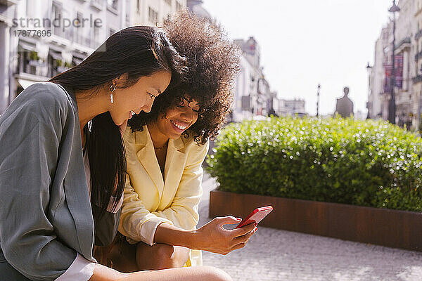 Smiling woman sharing smart phone with friend