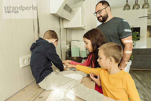 Lächelnder Vater mit Kindern  die in der Küche das Frühstück zubereiten