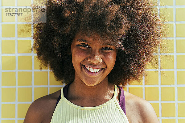 Glückliches Mädchen mit Afro-Frisur vor gelber Wand