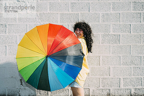 Glückliche Frau dreht an einem sonnigen Tag einen bunten Regenschirm