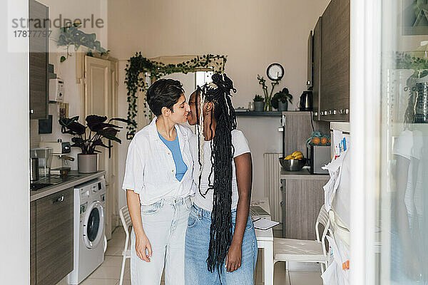 Lesbian couple kissing each other in kitchen at home