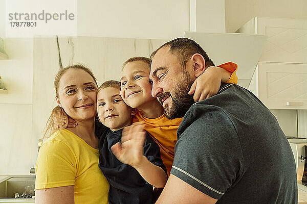 Glückliche Eltern umarmen ihre Söhne in der Küche
