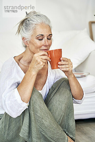Lächelnde Frau riecht zu Hause Kaffee in der Tasse