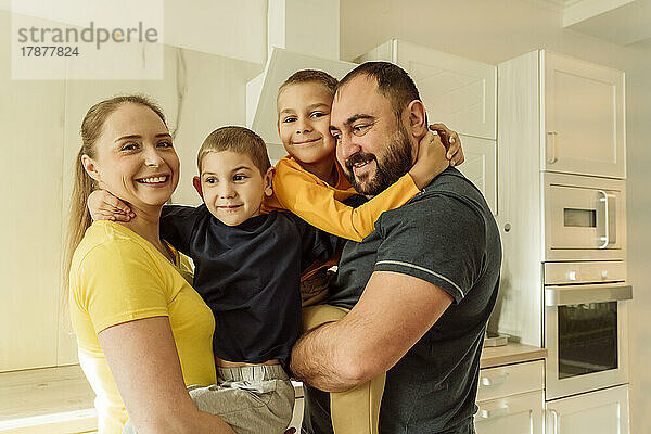 Lächelnde Eltern umarmen ihre Söhne in der Küche