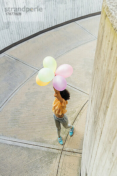 Verspielte Frau mit Luftballons steht auf Fußweg