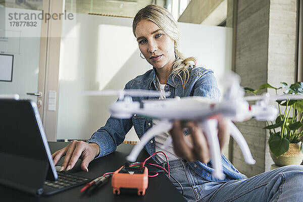 Blonde Frau hält Drohne mit Tablet-PC im Büro