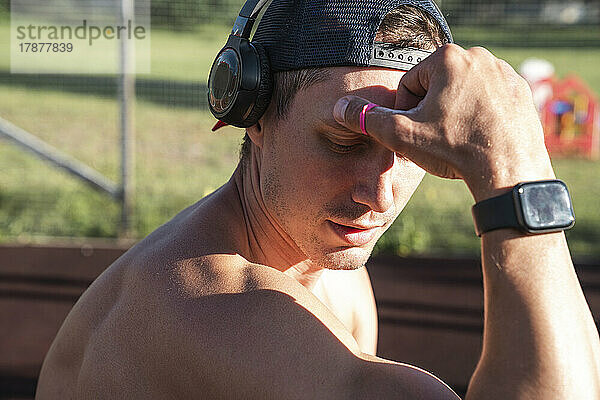 Nackter Oberkörper Athlet trägt eine Smartwatch und hört an einem sonnigen Tag Musik über kabellose Kopfhörer