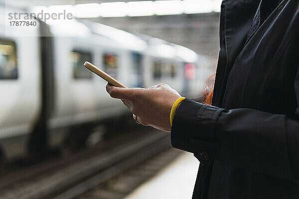 Hände einer Frau  die ihr Mobiltelefon am Bahnsteig benutzt