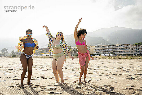 Sorglose  gemischtrassige Freunde tanzen an einem sonnigen Tag am Strand