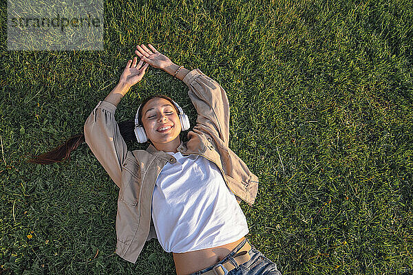 Smiling woman lying down and listening music at park