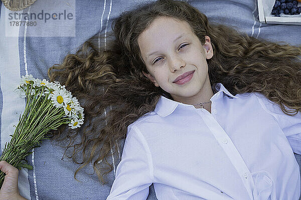 Mädchen hält Kamillenblüten auf einer Decke liegend