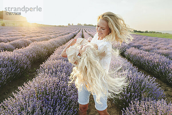 Happy mother spinning daughter in lavender field
