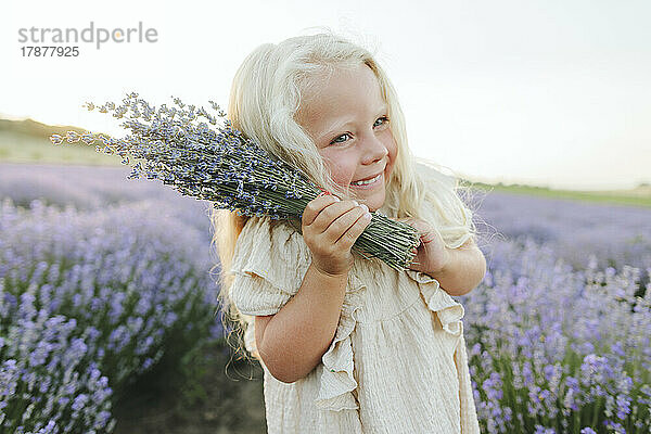 Smiling girl with lavender bouquet standing in field