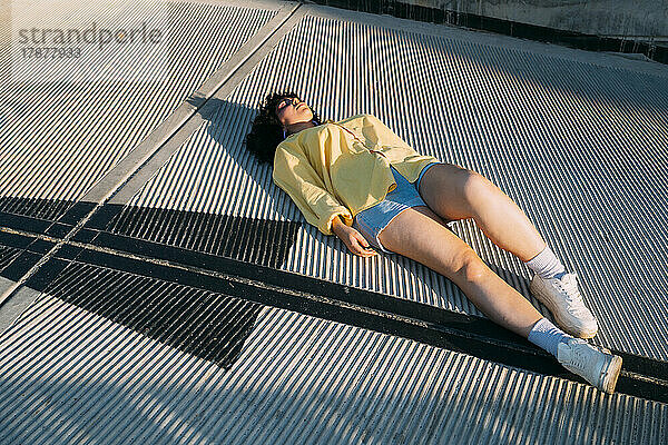 Junge Frau liegt an einem sonnigen Tag auf einem Fußweg
