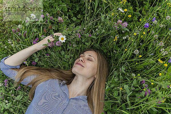 Smiling woman with eyes closed lying on grass at field