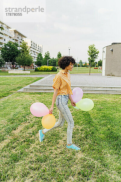 Junge Frau mit bunten Luftballons läuft auf Gras im Park