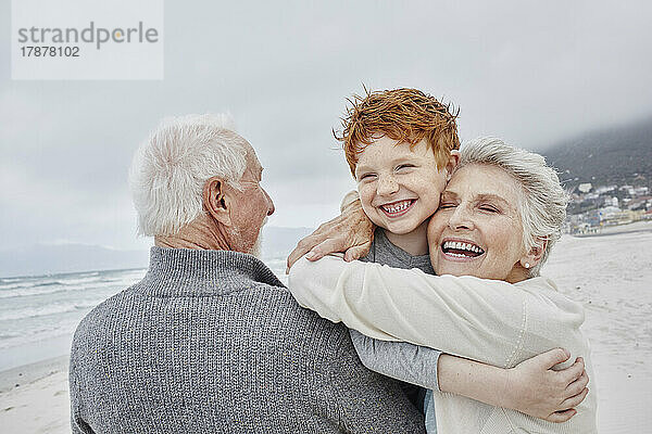 Caring grandparents embracing grandson on the beach