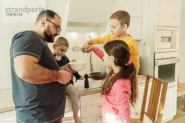 Vater mit Kindern bereitet Omelett in der Küche zu