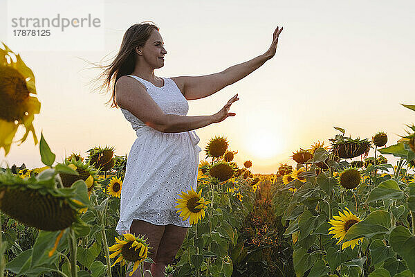 Lächelnde Frau gestikuliert auf Sonnenblumenfeld