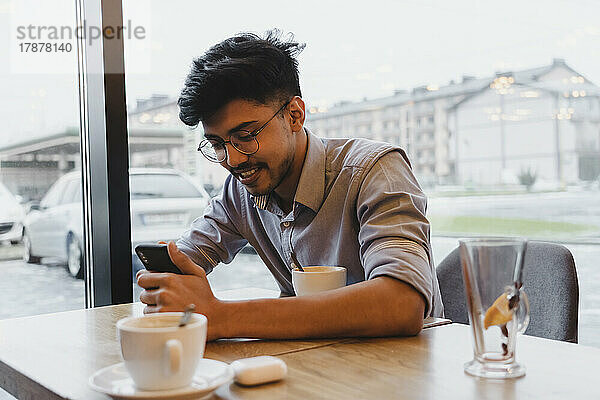 Glücklicher Mann benutzt Smartphone am Fenster im Café
