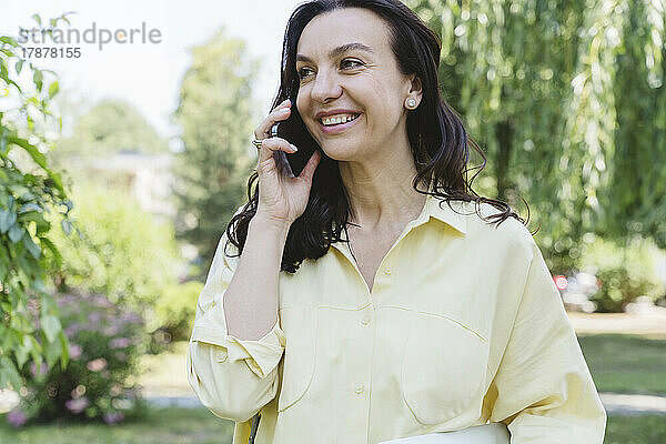 Glückliche Frau  die im Park mit dem Handy spricht