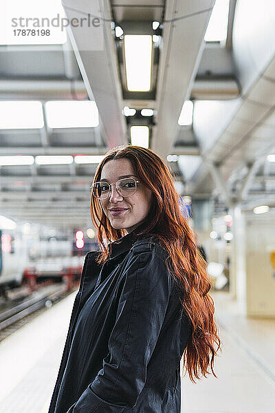 Glückliche rothaarige Frau steht am Bahnsteig