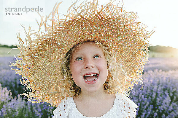 Cheerful girl wearing hat in field at sunset